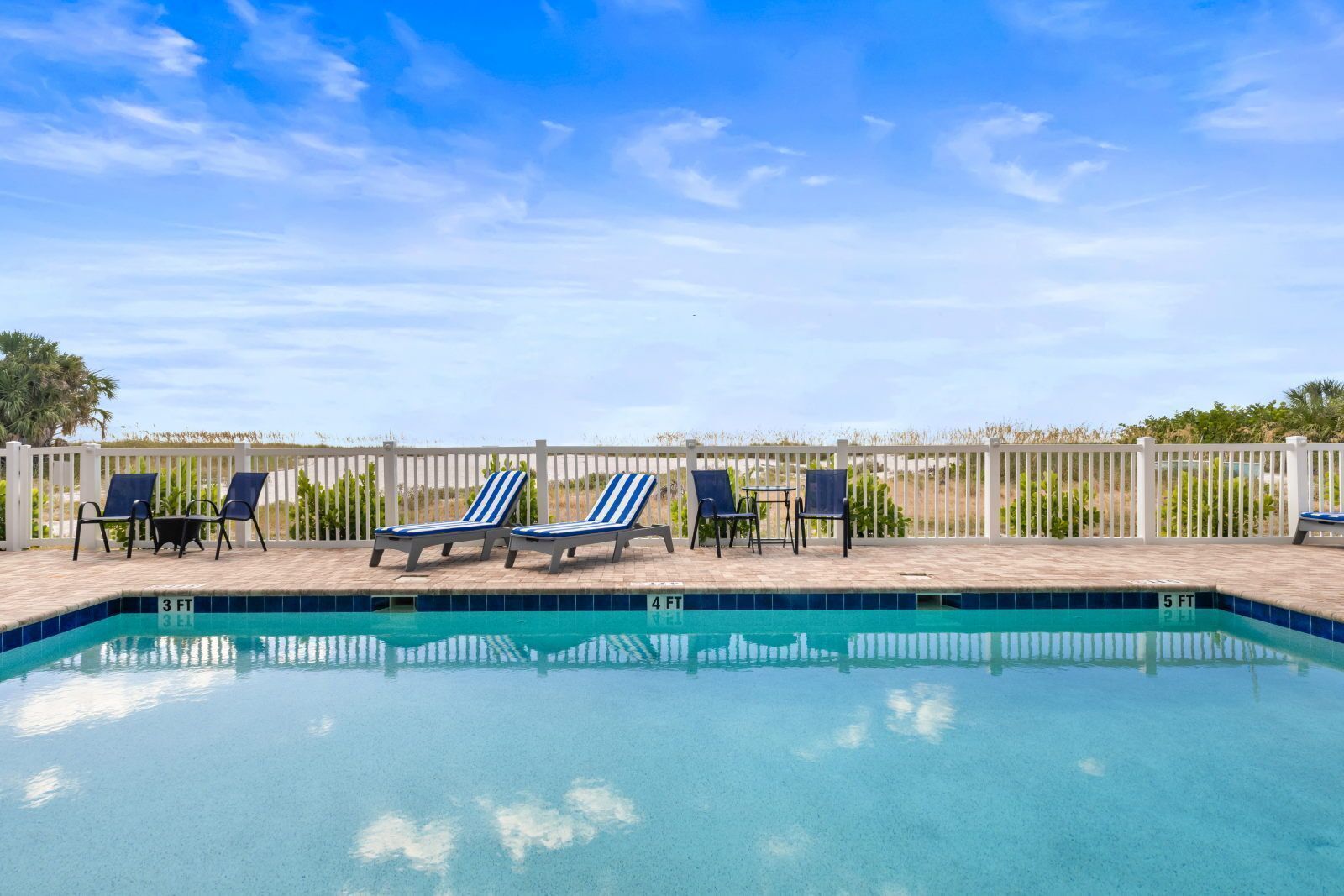 A swimming pool with lounge chairs and a white fence.