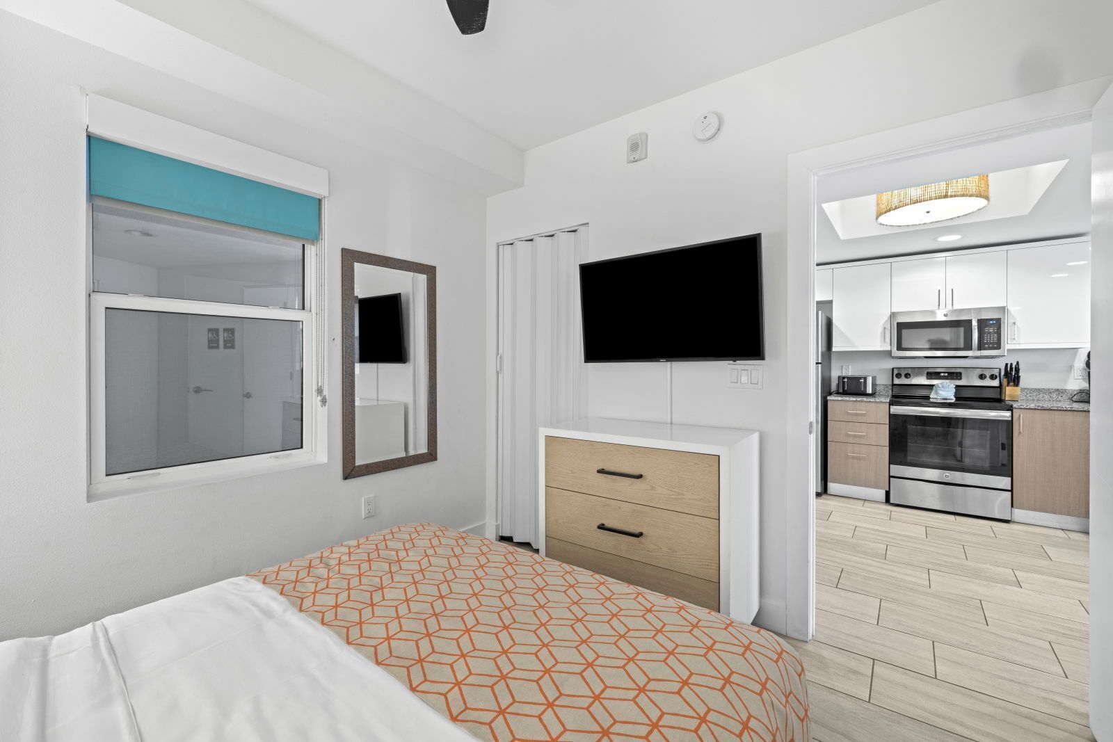Une chambre comprenant un lit, une télévision, un miroir, une armoire et un coin cuisine équipé d’un four à micro-ondes et d’un four traditionnel.