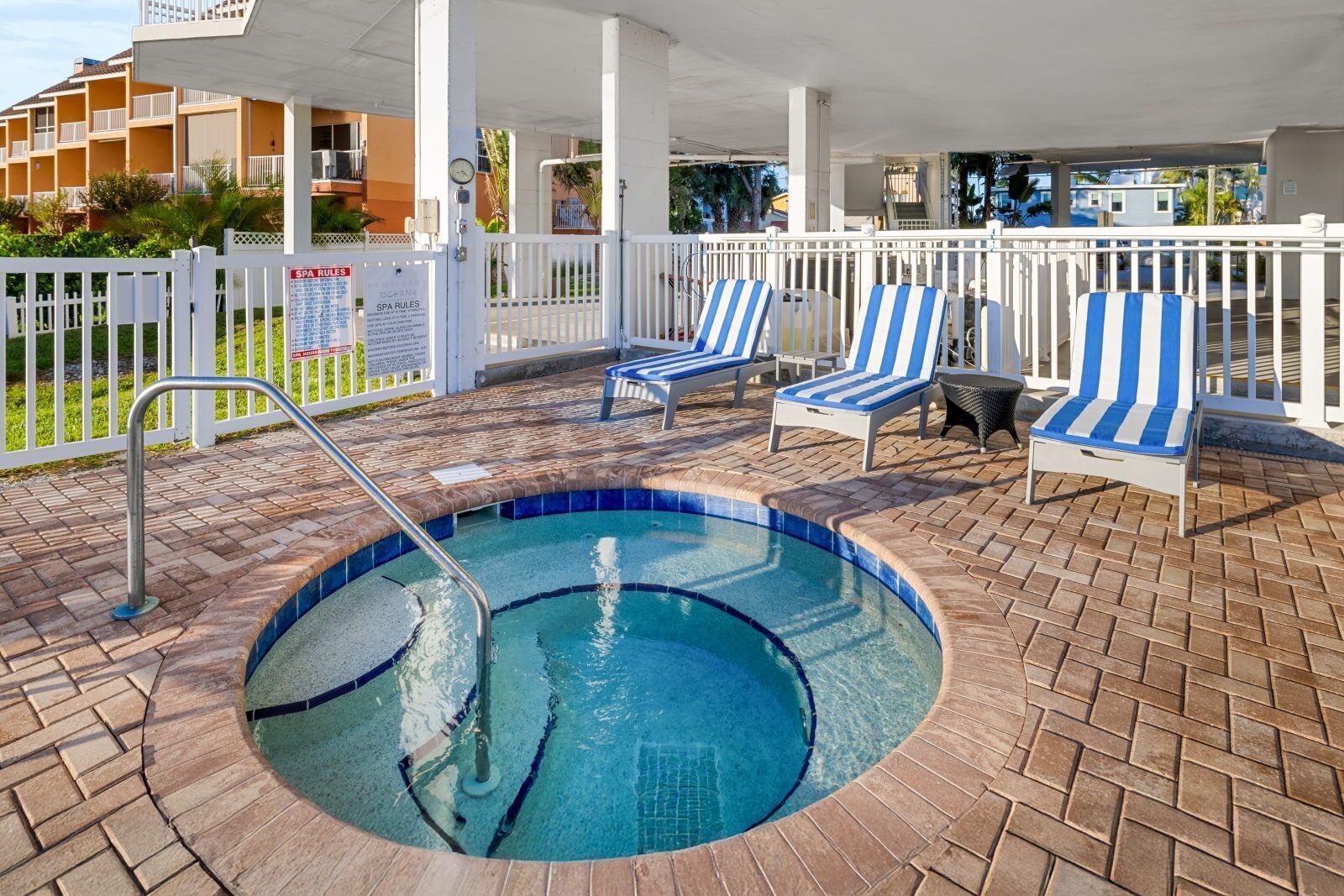 A pool area with a small pool, lounge chairs, and a white fence.