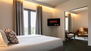 Ein Hotelzimmer mit Bett, Wandfernseher, Sessel und Tisch mit Gläsern und Flasche.