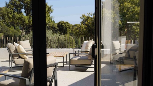 Un espace extérieur aménagé, protégé par des parois de verre, avec plusieurs fauteuils confortables et une table basse.