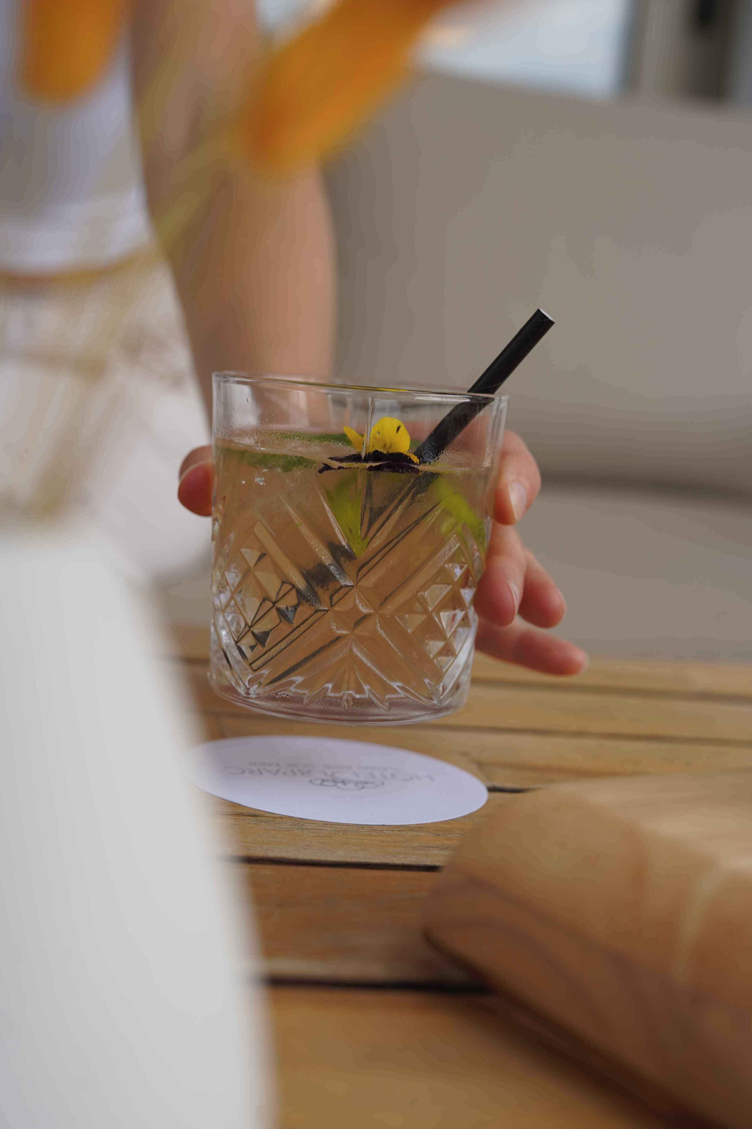 En hand håller i ett glas med ett sugrör, och glaset innehåller en dryck med en citronskiva och mynta.
