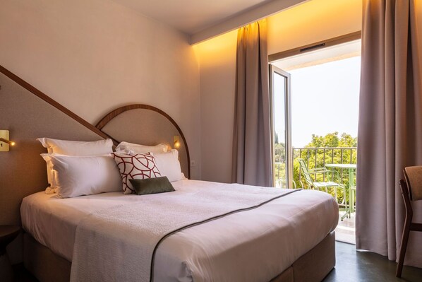 Une chambre d’hôtel comprenant un lit, une table de chevet, une fenêtre avec des rideaux et un balcon aménagé avec du mobilier d’extérieur.