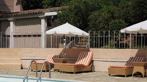 A swimming pool with lounge chairs and umbrellas, surrounded by a fence and greenery.