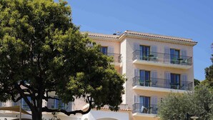 A multi-story building with balconies, surrounded by greenery and a clear sky.