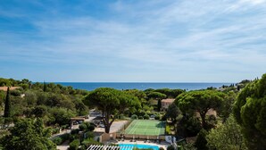A residential area with a tennis court, swimming pool, and a view of the sea.