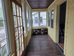Un porche cubierto con piso de madera, ventanas grandes y un zapatero.