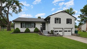 A two-story house with a garage, a well-maintained lawn, and a tree in the front yard. - Family Favorite_Arcades_ KingBeds_ Sleeps 10_ BBQ (Shawnee)