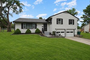A two-story house with a garage, a well-maintained lawn, and a tree in the front yard. - Cozy Home_Arcades_KingBeds_Sleeps 10_BBQ Grill (Shawnee)