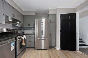 A modern kitchen with stainless steel appliances, grey cabinets, and a wooden floor. - Cozy Home_Arcades_KingBeds_Sleeps 10_BBQ Grill (Shawnee)