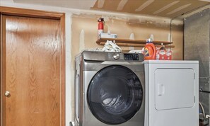 Un área de lavandería con lavadora y secadora, una puerta de madera y un estante con productos de limpieza.