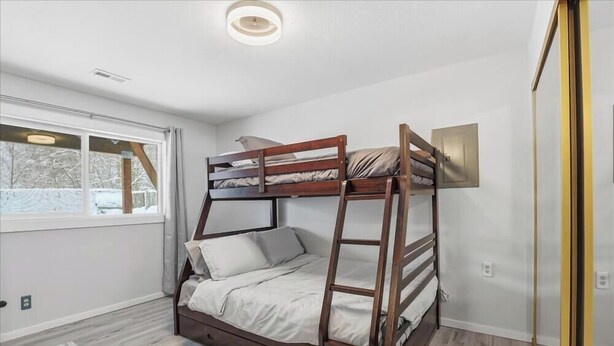 Une chambre avec un lit superposé, une fenêtre, une échelle et un luminaire fixé au mur.