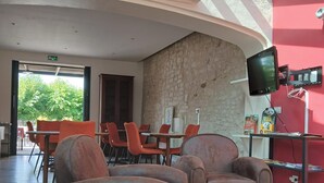 A lobby with a stone wall, a mounted TV, and orange chairs. - Au Bosquet Fleuri - Maison de campagne (Martizay)