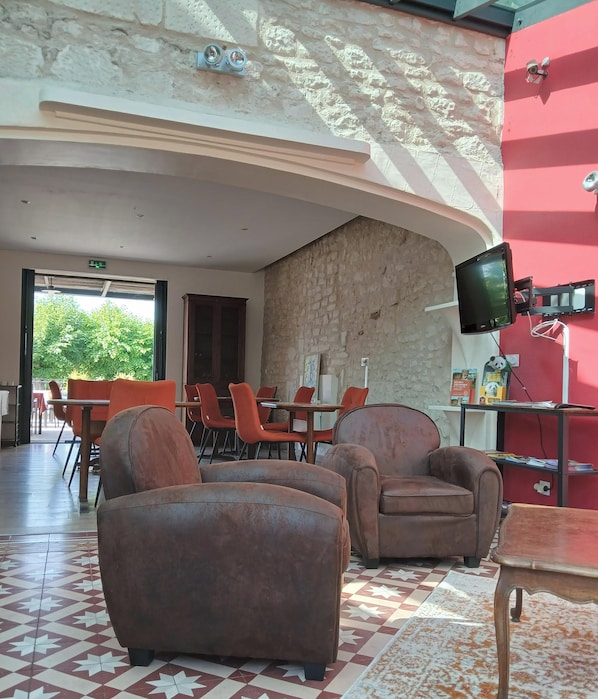 A lobby with a stone wall, a mounted TV, and orange chairs. - Au Bosquet Fleuri - Maison de campagne (Martizay)