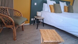 A room with a bed, a wicker chair, a small table, and a wooden stool. - Au Bosquet Fleuri - Maison de campagne (Martizay)