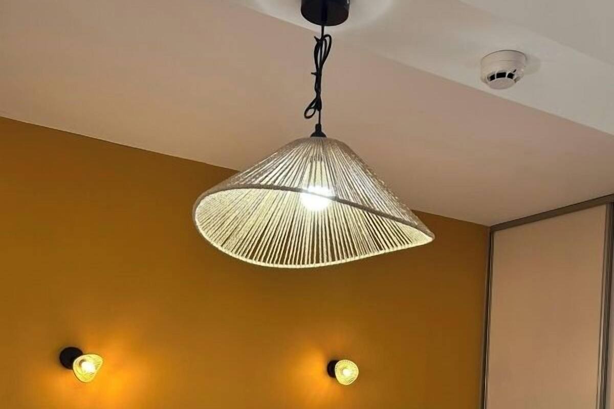 Habitación de hotel con cama, almohadas, una toalla doblada, lámpara colgante y apliques de pared.