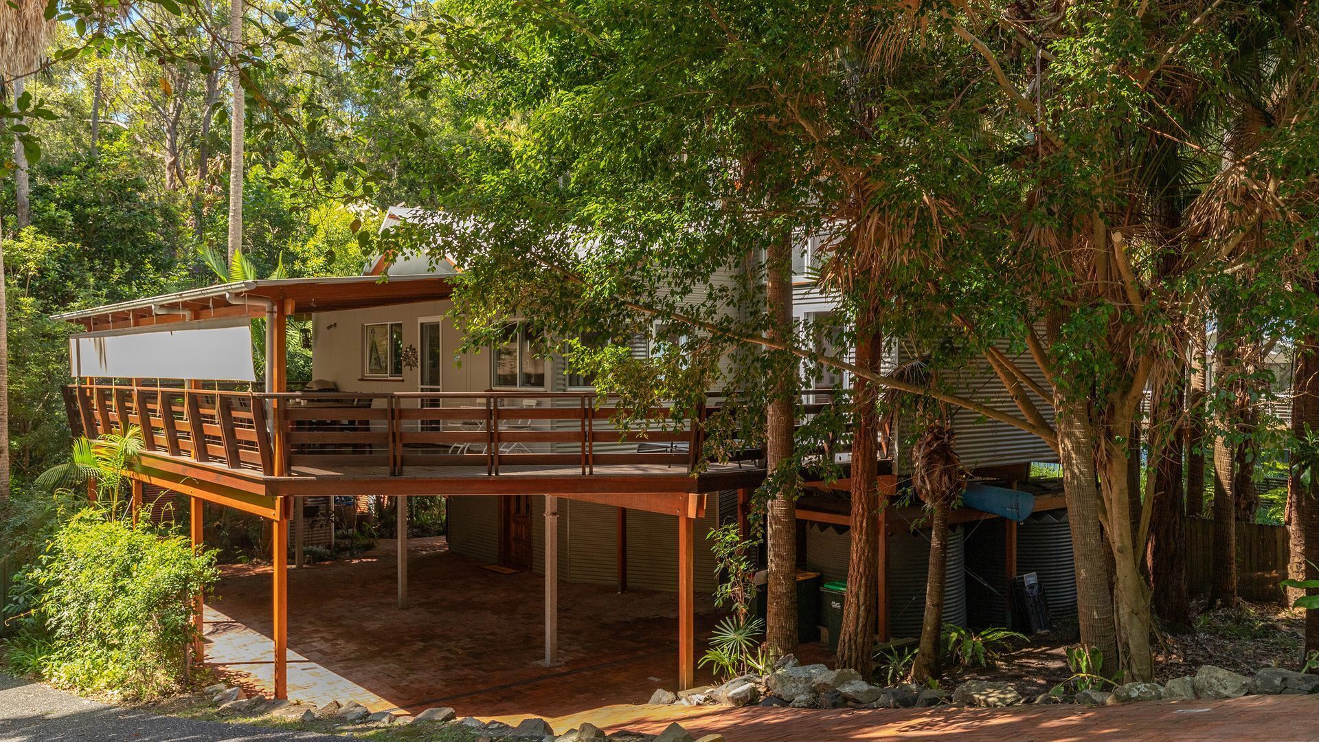 A house with a wooden deck, surrounded by dense foliage.