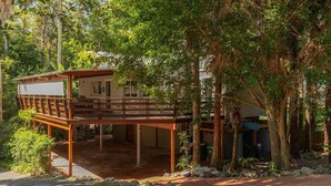 A house with a wooden deck, surrounded by dense foliage. - The Deck - short walk to Elizabeth Beach - sleeps 14 - outdoor spa (Elizabeth Beach)
