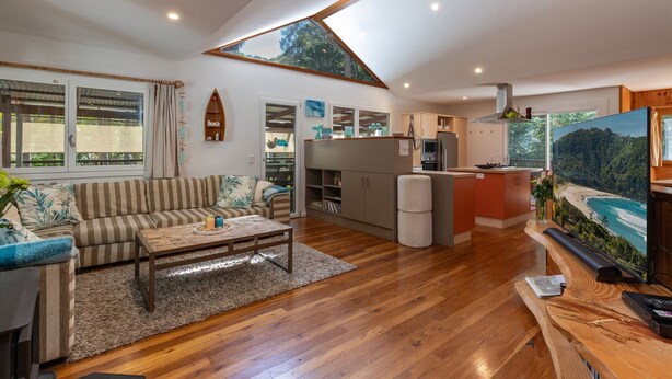 A modern living room with a sofa, coffee table, and a kitchen area with a view of a beach. - The Deck - short walk to Elizabeth Beach - sleeps 14 - outdoor spa (Elizabeth Beach)