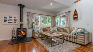 A cozy living room with a fireplace, striped sofa, and a coffee table. - The Deck - short walk to Elizabeth Beach - sleeps 14 - outdoor spa (Elizabeth Beach)