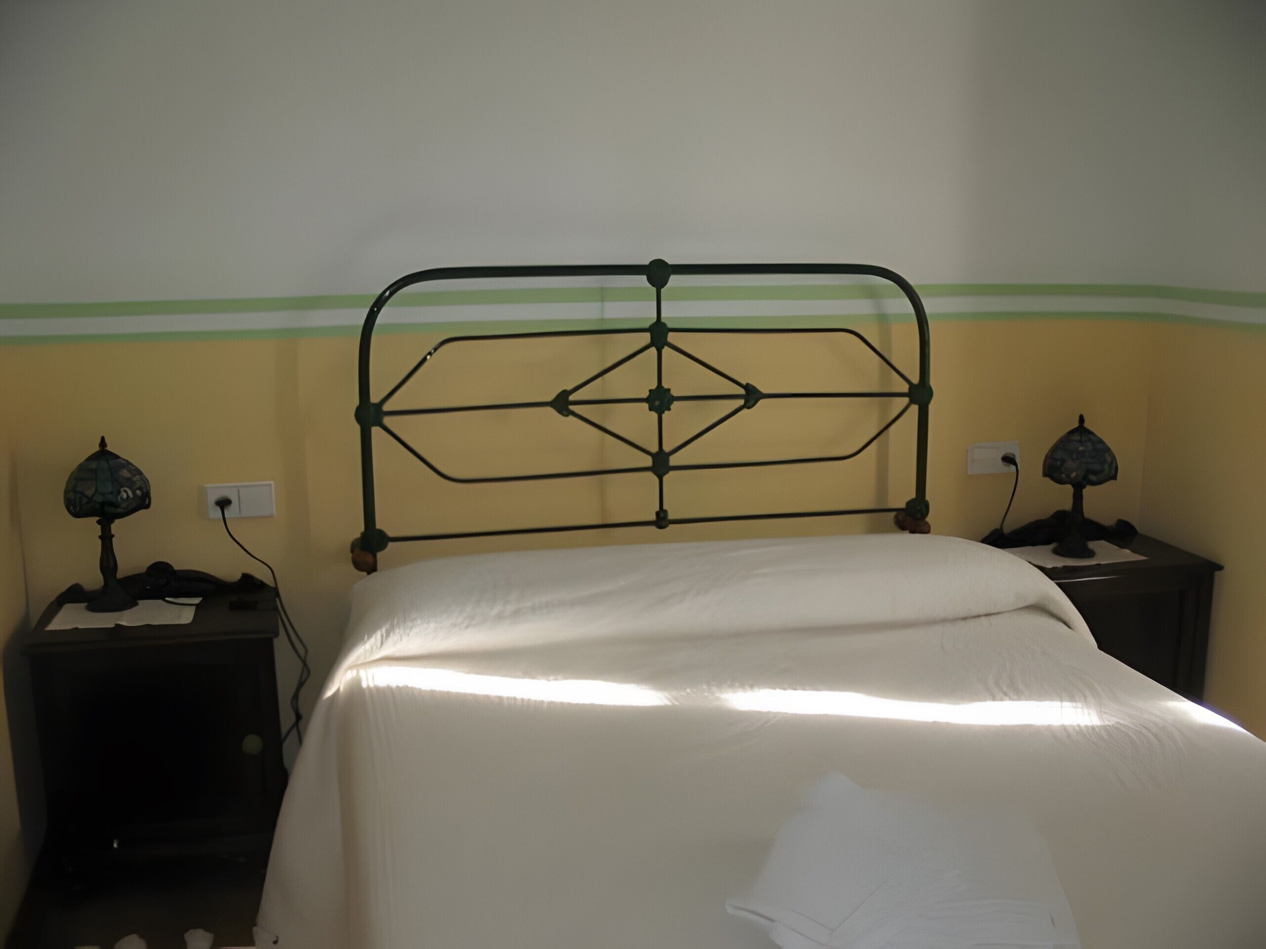 Een bed met een metalen hoofdbord, twee nachtkastjes met lampen, en een muur met een groene strook.
