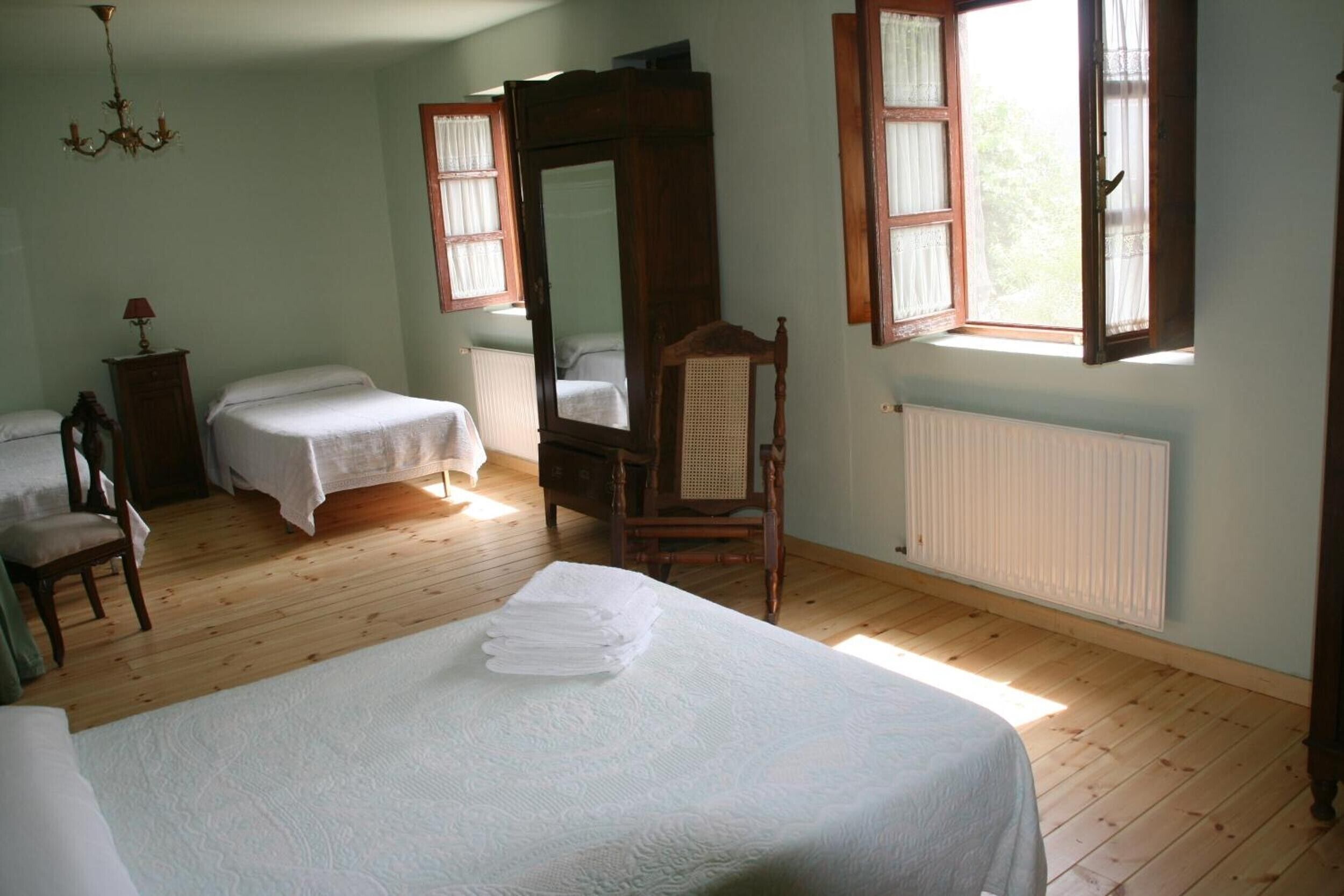 Una habitación con dos camas, piso de madera, un espejo grande y una ventana con cortinas.