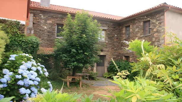 Un bâtiment en pierre avec un toit en tuiles, un banc en bois et diverses plantes.