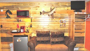 Une pièce compacte avec un mur en bois, une petite kitchenette, un canapé agrémenté de coussins à motifs et un téléviseur fixé au mur.