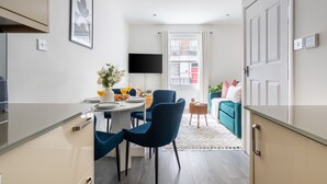 A modern kitchen with a dining area, a flat-screen TV, and a view of the street through a window. - Cosy 2BR in Marylebone Near Baker Street (London)