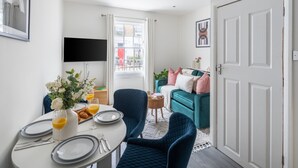 A dining area with a table set for two, a TV mounted on the wall, and a teal sofa in the background. - Cosy 2BR in Marylebone Near Baker Street (London)