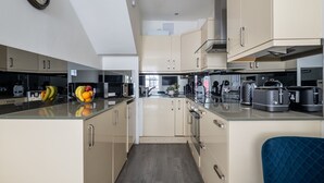 A modern kitchen with a central island, a clock on the wall, and a blue chair. - Cosy 2BR in Marylebone Near Baker Street (London)