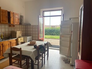 Una cocina con armarios de madera, una mesa de comedor con sillas, un refrigerador y una ventana con vistas a zonas verdes.