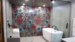 Une salle de bain moderne avec un mur de douche orné d’un motif floral, une baignoire sur pieds et un espace de douche délimité par des parois en verre.
