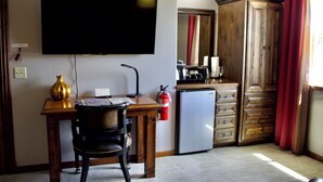 Une chambre d’hôtel équipée d’un bureau, d’une chaise, d’une télévision, d’un minibar et d’une armoire.