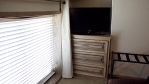 A bedroom with a bed, a TV, a dresser, and a window with blinds. - The Diamond Suite is our flagship luxury suite. (Fredericksburg)