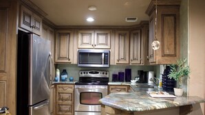 A kitchen with wooden cabinets, stainless steel appliances, a marble countertop, and a potted plant. - The Diamond Suite is our flagship luxury suite. (Fredericksburg)