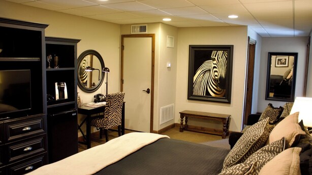 Une chambre d’hôtel équipée d’un lit, d’un bureau, d’une chaise, d’une armoire, d’un miroir et d’œuvres d’art accrochées aux murs.
