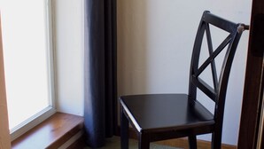 Une pièce d’angle avec une fenêtre, une chaise en bois sombre et un sol recouvert d’une moquette.