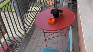 En balkon med et rødt bord, en blå stol, en potteplante og en lilla orchidé.