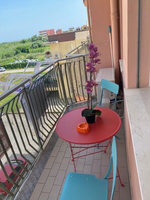 A balcony with a red table, a blue chair, a potted plant, and a purple orchid. - Fisch house (Chioggia)
