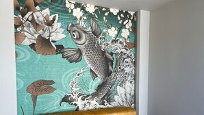 Et værelse med en guldgul sofa foran en væg med et stort, detaljeret kunstværk med fisk og blomster.