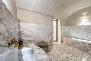 A marble bathroom with a bathtub, a small round table, and a door leading to another room. - Palais Arbaa (Marrakech)