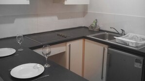 Een kleine keuken met witte kastjes, een zwart aanrecht en een kleine koelkast.