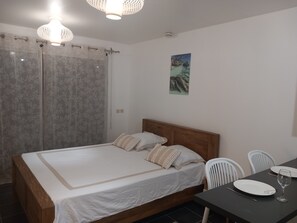 Ein Schlafzimmer mit Bett, einem Esstisch mit Stühlen, einem Bild an der Wand und einem Fenster mit Vorhängen.