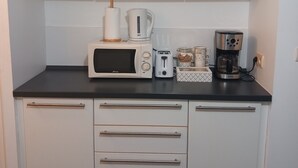 Een kleine keuken met witte kastjes, een magnetron, broodrooster, koffiezetapparaat en een keukenrol.