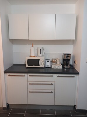 Eine Küche mit weißen Schränken, einer Mikrowelle, einem Toaster, einer Kaffeemaschine und einer Küchenpapierrolle.