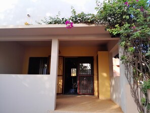 Une entrée de maison avec une porte grillagée, un petit porche et un mur recouvert de plantes grimpantes.