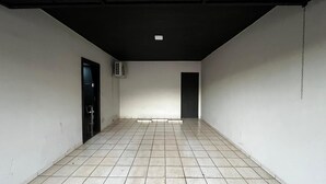 Un pasillo con suelo de baldosas, una puerta negra y una pared blanca con una lámpara en el techo.