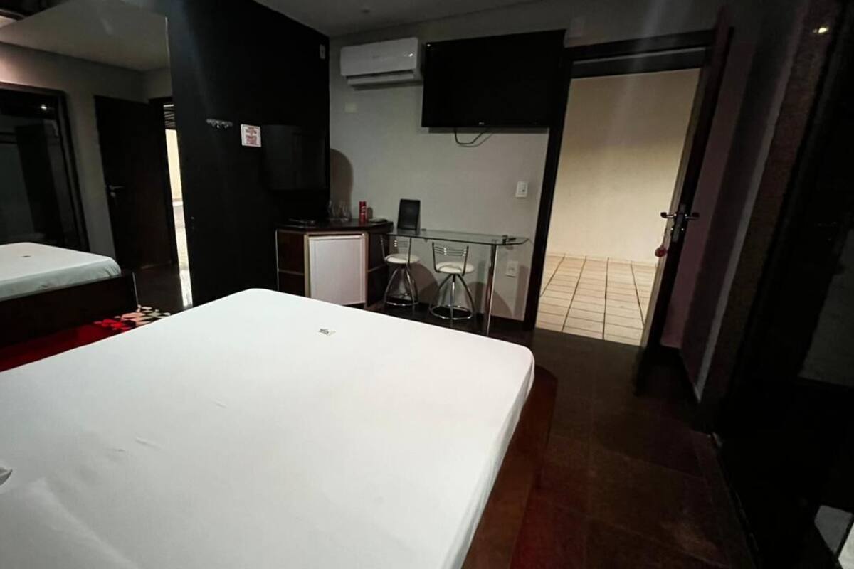 A hotel room with a bed, a small desk with a chair, a TV, and an air conditioning unit.
