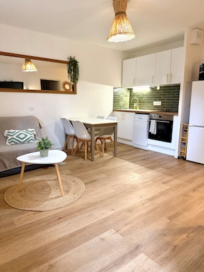 Eine moderne Küche mit weißen Schränken, ein Essbereich mit rundem Tisch und Stühlen sowie ein Wohnzimmer mit einer Couch und einem Couchtisch.